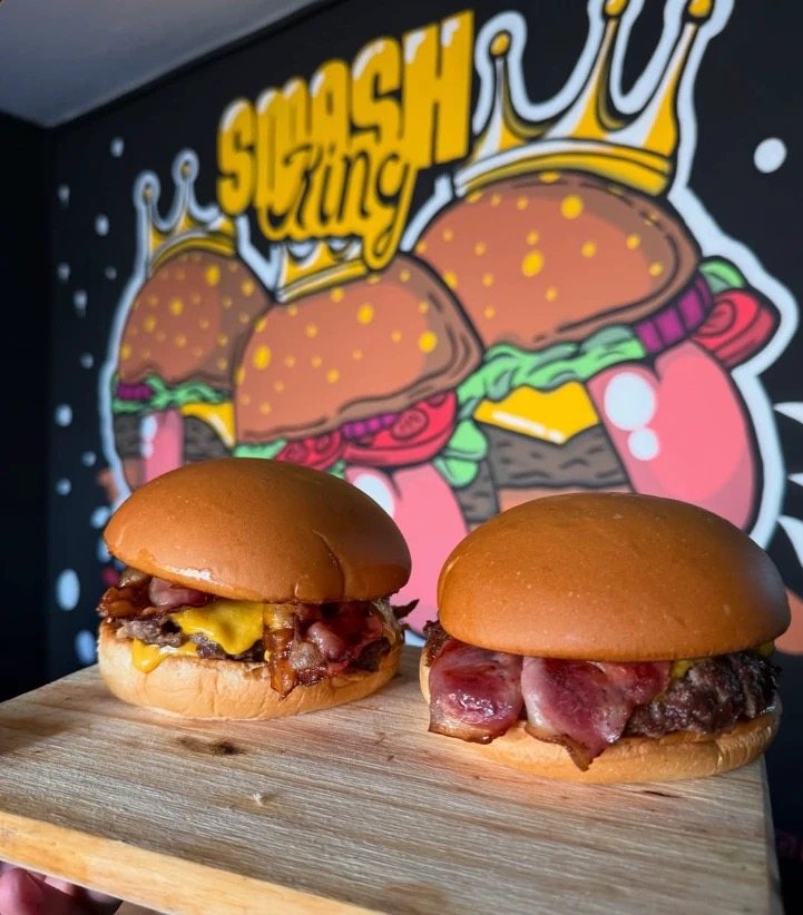 Dos smash burgers con bacon y cheddar frente al mural de Smash King en el local de Luzuriaga